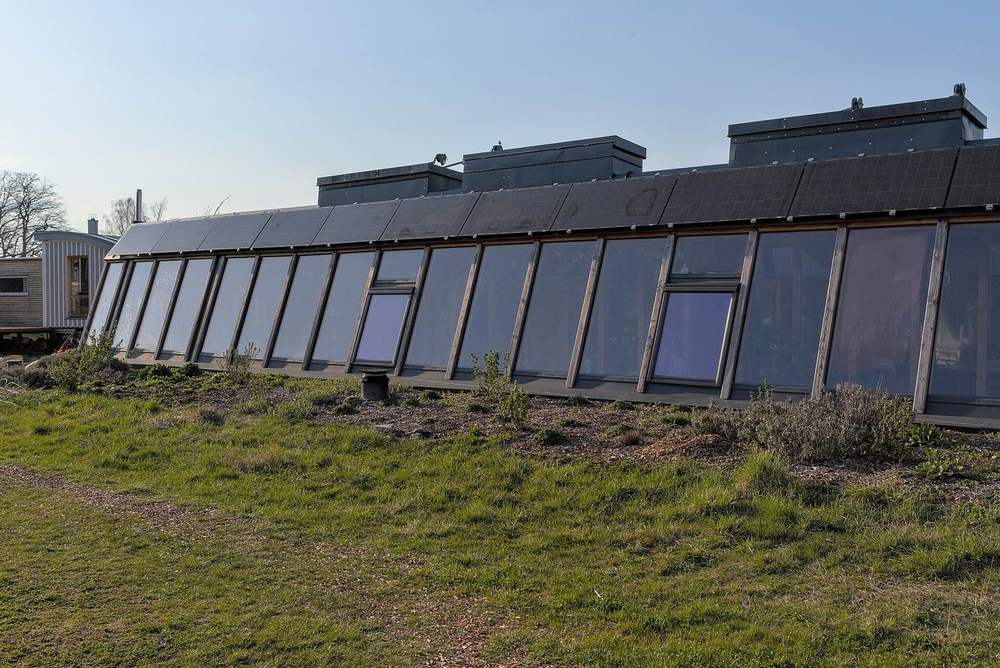 An Earthship with a long glass front wall facing the sun and solar panels along its roofline