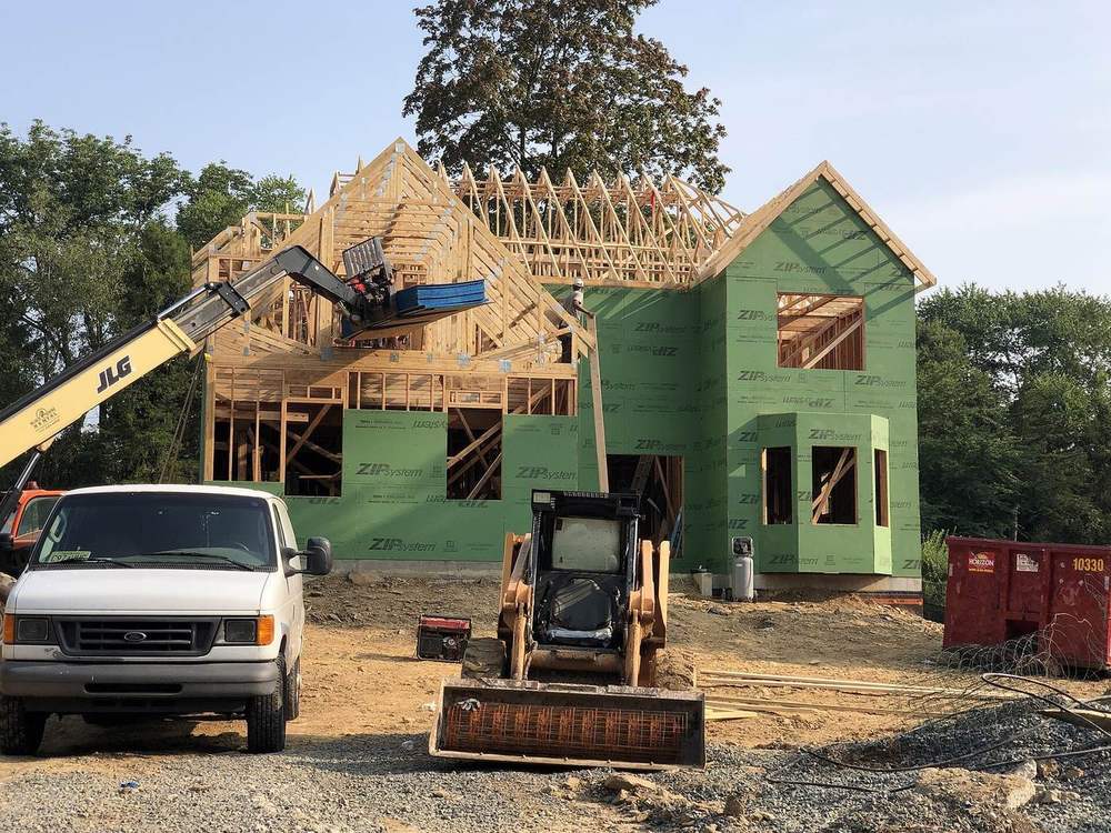 A new wood-frame house wrapped in green sheathing, with a lift and a skid steer on the lot