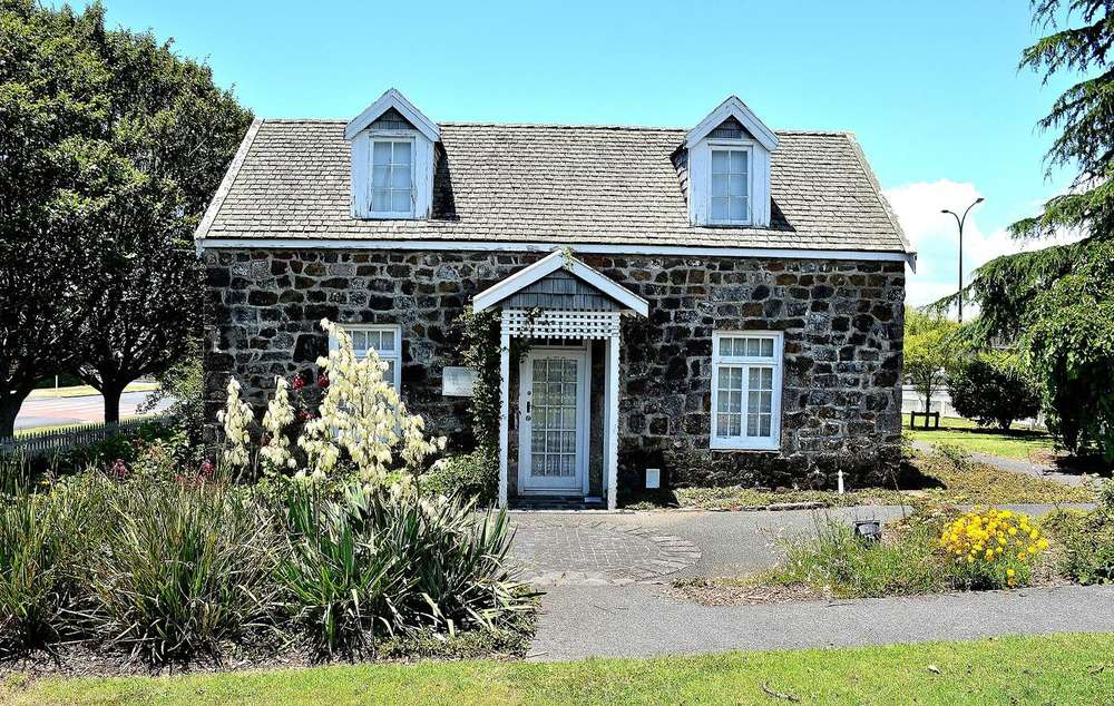 A small dark basalt stone cottage with white window frames and dormers